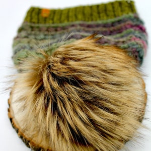 May include: A brown faux fur pom pom for a hat. The pom pom is on a wooden surface.