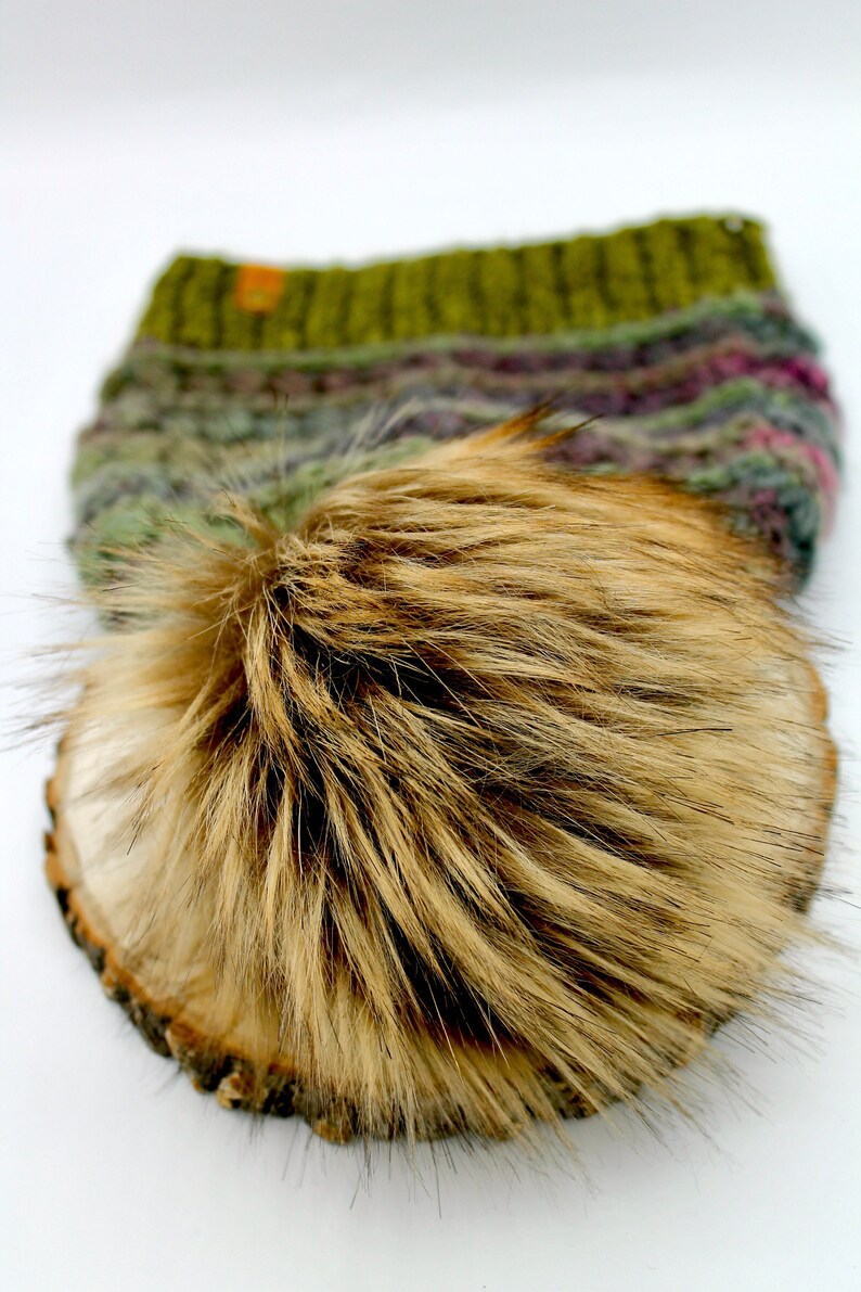 May include: A brown faux fur pom pom for a hat. The pom pom is on a wooden surface.