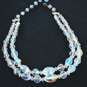 May include: A double strand iridescent crystal necklace with a silver clasp. The necklace is made of faceted oval-shaped crystals.