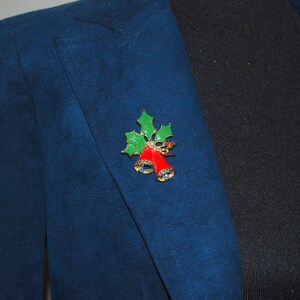 May include: A gold-tone Christmas brooch with red bells and green holly leaves. The brooch is adorned with sparkling rhinestones.