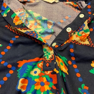 May include: A navy blue shirt with a colorful paisley print. The shirt has a button-up collar and a button closure.
