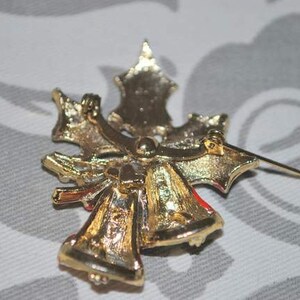 May include: Gold-tone Christmas tree brooch with red and white enamel accents. The brooch features two bells and a bow.