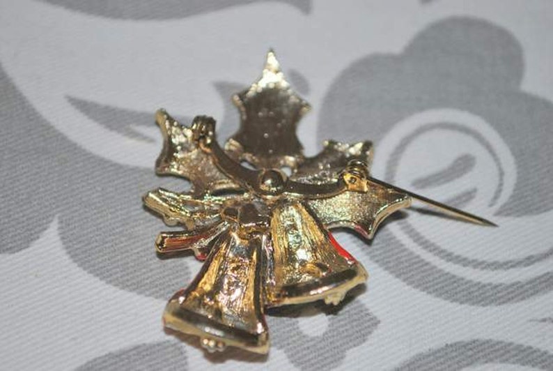 May include: Gold-tone Christmas tree brooch with red and white enamel accents. The brooch features two bells and a bow.