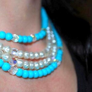 May include: A layered necklace with turquoise and white beads. The necklace is made of multiple strands of beads, including turquoise, white, and clear crystal beads.