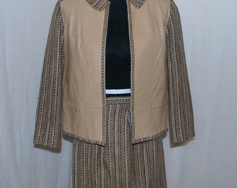 May include: A brown and beige tweed skirt suit with a leather vest. The jacket has a collar and long sleeves. The skirt is knee-length and has a straight silhouette.