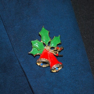 May include: A gold-tone Christmas pin with red bells and green holly leaves. The bells have blue rhinestones and a white pearl accent.