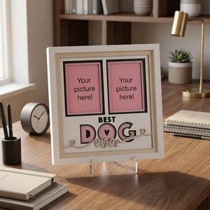 May include: A square white picture frame with a light wood inner border containing two vertical photo slots with pink backgrounds. The frame features the text BEST DOG ever in black and pink lettering with small heart accents at the ends.