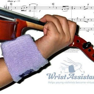 May include: A young violinist wearing a purple wristband practices playing a violin. The violin is brown with a black fingerboard and a scroll. The image includes sheet music with the word "Allegro" and musical notes. The text "Wrist Assistant" is visible in the lower right corner of the image. The text "Helps young violinists become virtuosos!" is below the "Wrist Assistant" text.