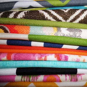 May include: A stack of colorful fabric swatches with various patterns, including geometric, floral, and abstract designs. The fabrics are folded neatly and arranged in a vertical stack.