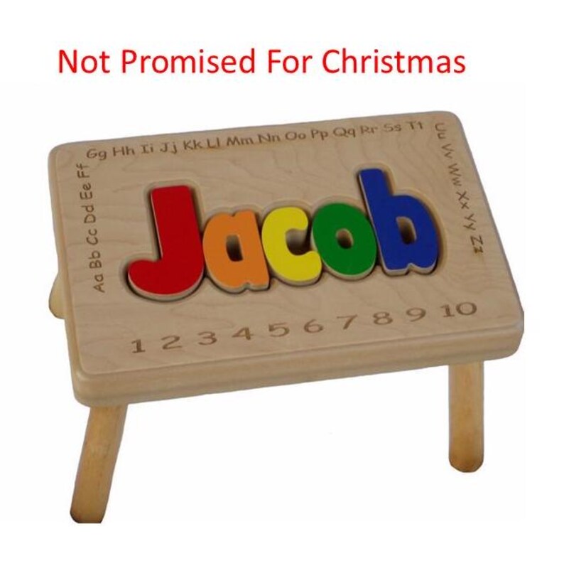 Pode incluir: Banco de madeira com um quebra-cabe&ccedil;a de nome personalizado no topo. O nome "Jacob" &eacute; escrito em letras coloridas. O banco tem quatro pernas e os n&uacute;meros de 1 a 10 est&atilde;o gravados no topo.