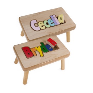 May include: Two wooden children's stools with personalized names. The top stool has the name "Cecelia" spelled out in pastel colors. The bottom stool has the name "Bryden" spelled out in rainbow colors.