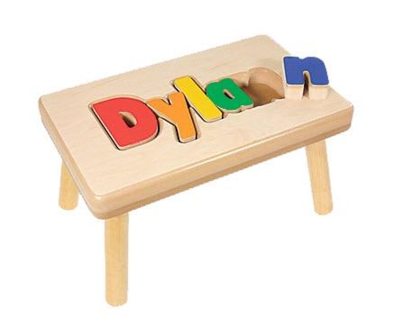 Pode incluir: Um banquinho de madeira com um recorte para o nome "Dylan" em letras coloridas. As letras s&atilde;o remov&iacute;veis e podem ser usadas como um quebra-cabe&ccedil;a.