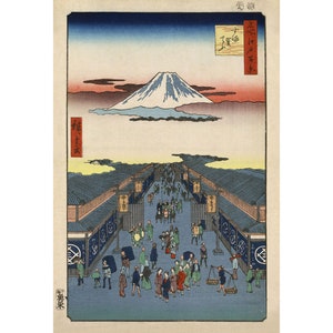 May include: A woodblock print depicting Mount Fuji in the distance, with a bustling street scene in the foreground. The street is lined with shops and people are walking and shopping. The print is in shades of blue, green, and red.