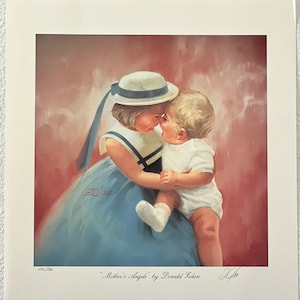 May include: A framed print of a painting titled "Mother's Angels" by Donald Zolan. The artwork depicts two children, one in a blue dress and a white hat with a blue ribbon, embracing a baby in a white outfit. The background is a soft, reddish-pink.