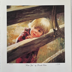 May include: A print titled "Rodeo Girl" by Donald Zolan. The artwork depicts a young child with blonde hair, wearing a red plaid shirt, leaning on a wooden fence. The print is numbered 575/850.