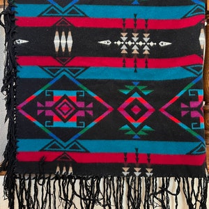 May include: A black blanket with a Southwestern geometric pattern in teal, red, purple, and green. The blanket has a fringe trim in black. The design includes diamond and triangle shapes.