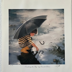 May include: A print titled "Touching the Sky" by Donald Zolan. It depicts a child in a yellow and brown striped shirt and tan boots, holding a black umbrella and touching a puddle. The image has a reflective quality.