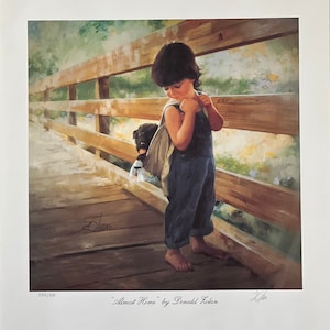 May include: A print titled "Almost Home" by Donald Zolan. It depicts a young child in denim overalls on a wooden bridge, carrying a small black dog in a bag. The artwork has a soft, painterly style with warm tones and a focus on the child's expression.
