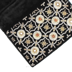 May include: Black velvet clutch with an embroidered floral design. The design features white, gold, and brown accents, creating a decorative border. The clutch is rectangular and appears to be closed.