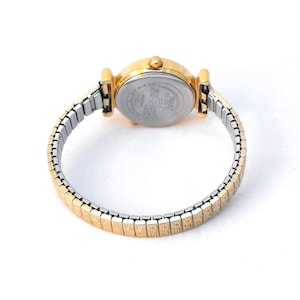 The gold-tone, stretch watch band is 8mm wide at the lugs, tapering to 6mm at the center back.