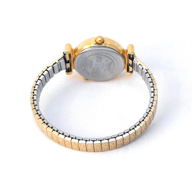 The gold-tone, stretch watch band is 8mm wide at the lugs, tapering to 6mm at the center back.