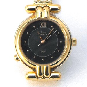 This is a fashionable gold-tone timepiece with quartz movement, featuring a round black dial with small dot markers and Roman number XII.