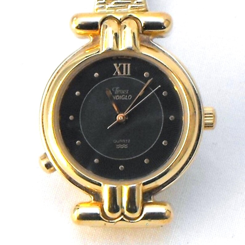 This is a fashionable gold-tone timepiece with quartz movement, featuring a round black dial with small dot markers and Roman number XII.