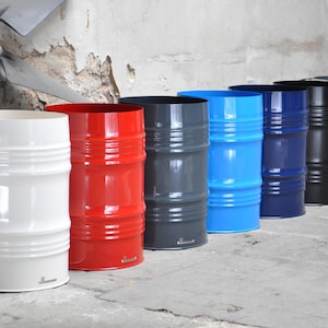 May include: A row of seven colorful metal barrel-shaped containers. The colors include white, red, gray, blue, navy, black, and silver. Each container has horizontal ridges and a smooth, glossy finish. The containers are lined up against a textured wall.