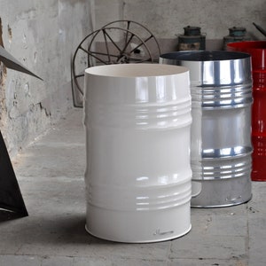 May include: Three industrial-style metal barrels in a concrete room. One is white, one is silver, and the third is red. Each barrel has horizontal ridges and a cylindrical shape, suggesting a modern, minimalist design.