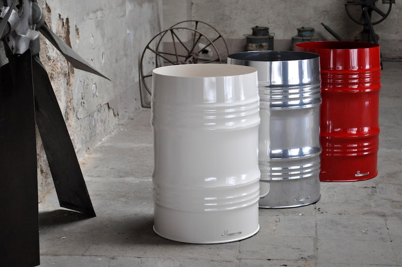 May include: Three industrial-style metal barrels in a concrete room. One is white, one is silver, and the third is red. Each barrel has horizontal ridges and a cylindrical shape, suggesting a modern, minimalist design.