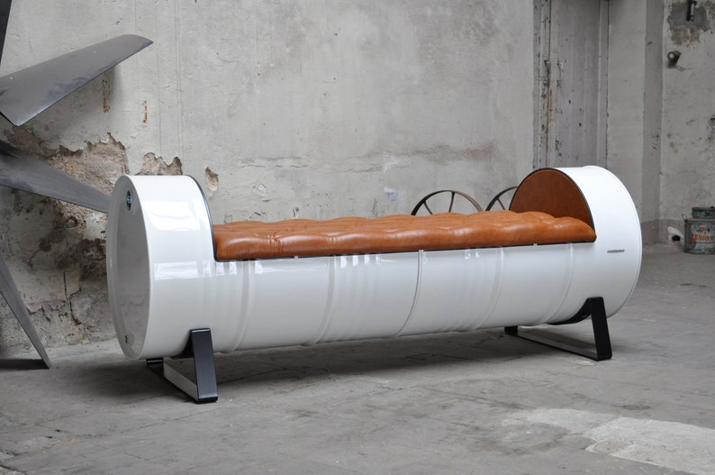 May include: A unique, industrial-style bench made from a repurposed white metal drum. It features a tufted, brown leather seat and black metal legs. The bench is a distinctive piece of furniture.
