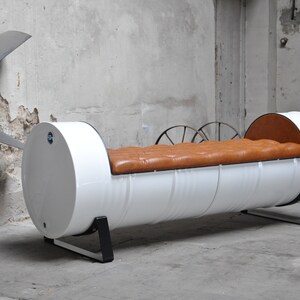May include: A unique, industrial-style bench made from a repurposed white barrel. The bench features a tufted, brown leather seat and is supported by black metal legs. The design is a blend of modern and rustic aesthetics.