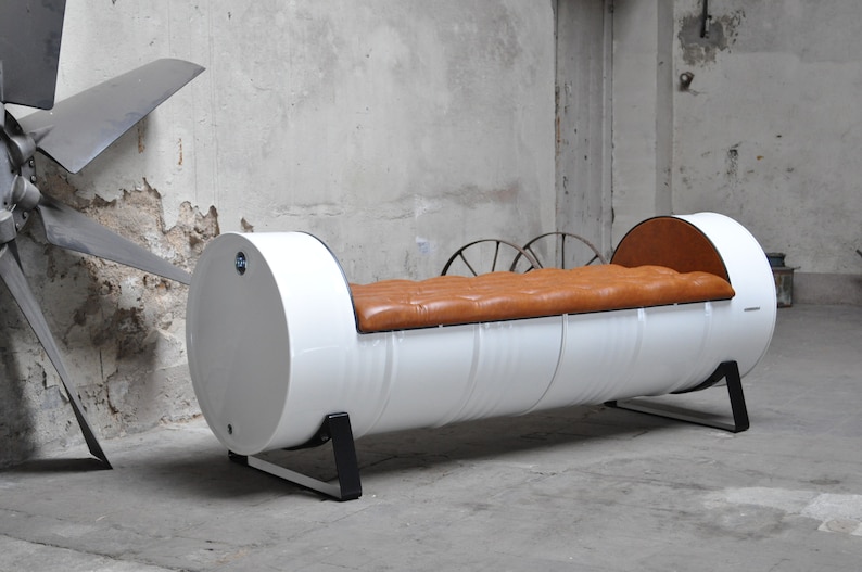 May include: A unique, industrial-style bench made from a repurposed white barrel. The bench features a tufted, brown leather seat and is supported by black metal legs. The design is a blend of modern and rustic aesthetics.