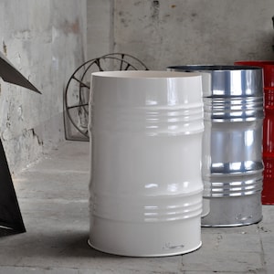 May include: Three industrial-style metal barrels, painted white, silver, and red, stand in a concrete room. The barrels have horizontal ridges and a glossy finish. The white barrel is in the foreground.