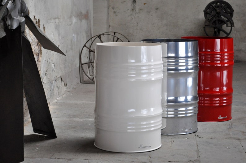 May include: Three industrial-style metal barrels, painted white, silver, and red, stand in a concrete room. The barrels have horizontal ridges and a glossy finish. The white barrel is in the foreground.