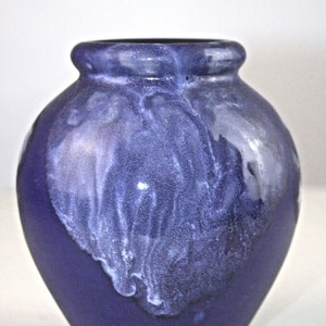 Könnte beinhalten: Eine kleine, runde, violette Keramikvase mit weißen Glasur-Akzenten. Die Vase hat eine glatte, glänzende Oberfläche.
