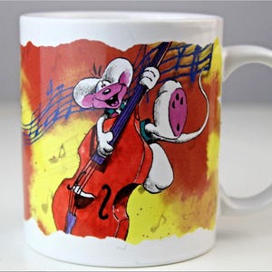 Könnte beinhalten: Weiße Keramiktasse mit einer Cartoon-Maus, die einen roten Kontrabass spielt. Die Maus hat eine rosa Nase und Ohren, vor einem Hintergrund aus Gelb, Orange und Rot mit Noten.