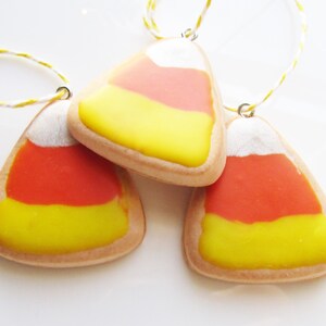 Puede incluir: Tres galletas con forma de ma&iacute;z dulce con glaseado blanco, naranja y amarillo. Las galletas est&aacute;n enhebradas en una cuerda y est&aacute;n listas para colgarse como adornos.