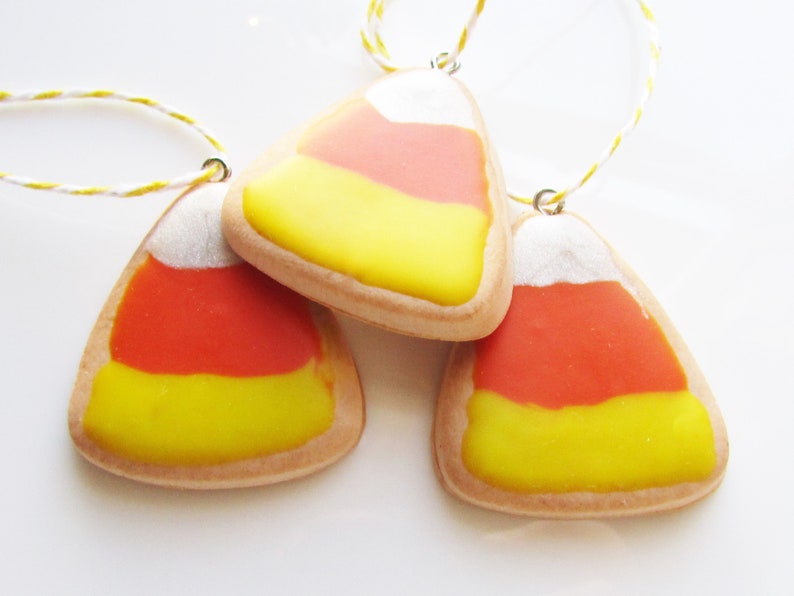 Puede incluir: Tres galletas con forma de ma&iacute;z dulce con glaseado blanco, naranja y amarillo. Las galletas est&aacute;n enhebradas en una cuerda y est&aacute;n listas para colgarse como adornos.