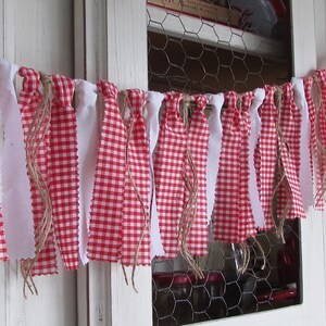 May include: A decorative banner featuring alternating red and white gingham and solid white fabric strips. The strips are attached to a natural twine, creating a rustic, country-style aesthetic. The banner is suitable for home decor.