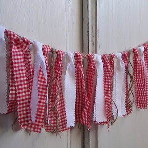 May include: A decorative banner featuring alternating red and white gingham fabric strips and solid white fabric strips. The banner is strung together with twine, creating a rustic and charming aesthetic. Perfect for festive occasions.