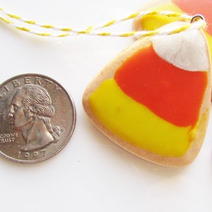 Puede incluir: Tres galletas con forma de ma&iacute;z dulce amarillo, naranja y blanco con una cuerda blanca atada a la parte superior.