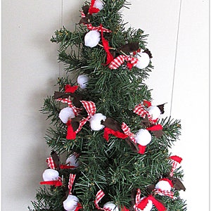 May include: A small artificial Christmas tree decorated with white pom-poms, red and white striped ribbons, and dark brown fabric accents. The tree has green needles and is set against a white background. A festive holiday decoration.