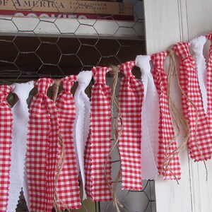 May include: A decorative banner featuring alternating red and white fabric strips. The red fabric has a classic gingham pattern, while the white strips have a scalloped edge. The banner is strung with twine, creating a rustic, country-style aesthetic.
