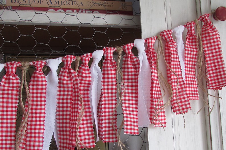 May include: A decorative banner featuring alternating red and white fabric strips. The red fabric has a classic gingham pattern, while the white strips have a scalloped edge. The banner is strung with twine, creating a rustic, country-style aesthetic.