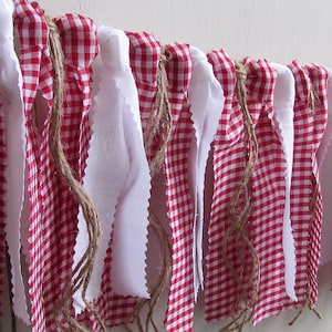 May include: A decorative banner featuring alternating red and white gingham fabric and white fabric strips. The banner is strung on a natural twine rope, creating a rustic and charming aesthetic. Perfect for festive occasions or home decor.