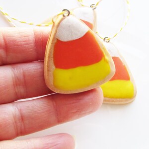 Puede incluir: Tres galletas hechas a mano con forma de ma&iacute;z dulce con glaseado blanco, naranja y amarillo. Las galletas est&aacute;n enhebradas en un cordel y est&aacute;n listas para colgarse como adornos.