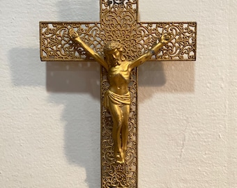 Peut inclure: Un crucifix en métal doré avec un motif de filigrane détaillé. La figure de Jésus-Christ est également dorée et est fixée à la croix.