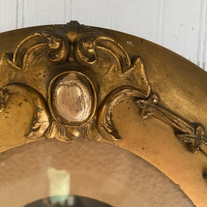 May include: A gold oval picture frame with ornate detailing around the edge. The frame has a raised, textured center with a gold finish.