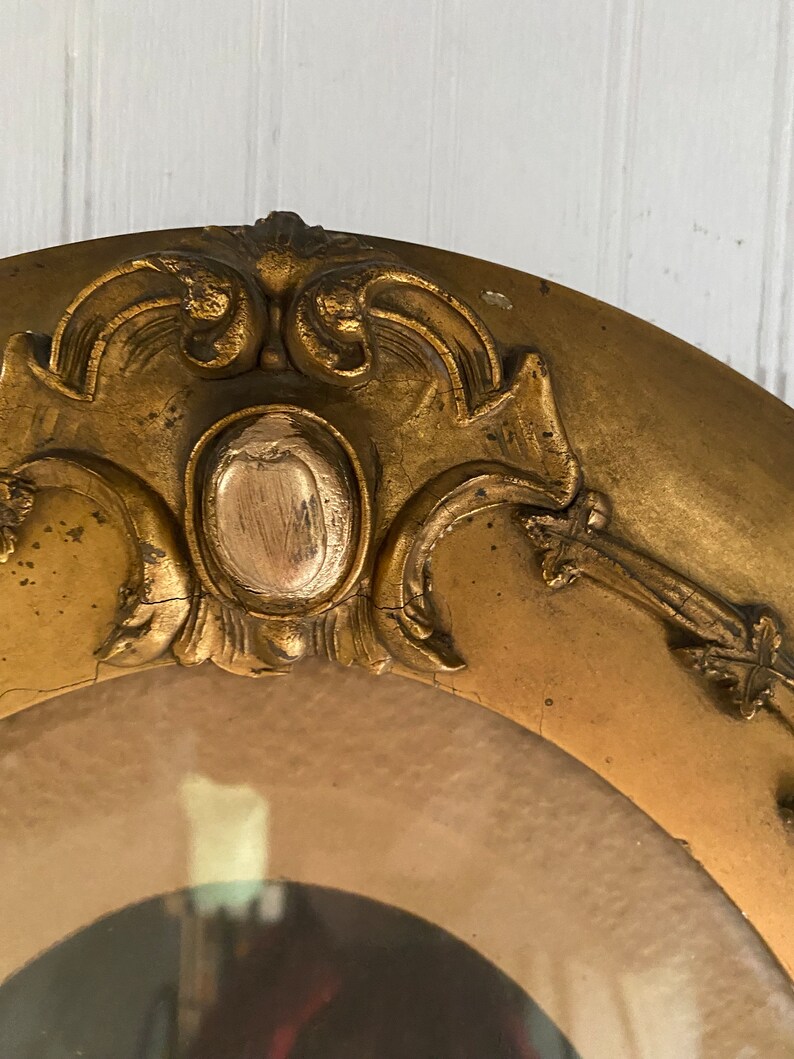 May include: A gold oval picture frame with ornate detailing around the edge. The frame has a raised, textured center with a gold finish.